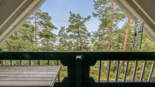 A wooden deck with a table and benches, overlooking a forested area with tall trees. - Kotkanpesä by Interhome (Masku)