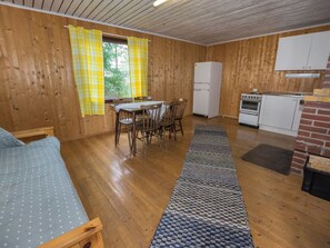 A compact room with wooden walls, a dining table with chairs, a refrigerator, an oven, and a bed with a blue polka dot cover. - Kotkanpesä by Interhome (Masku)