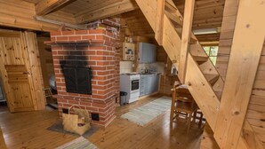 A cozy cabin interior with a brick fireplace, wooden floors, a kitchen area, and a staircase. - Kotkanpesä by Interhome (Masku)