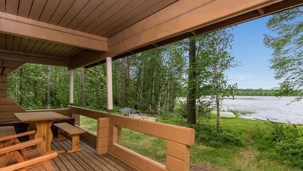 Una terraza de madera con bancos y una mesa, con vistas a un río y un bosque.
