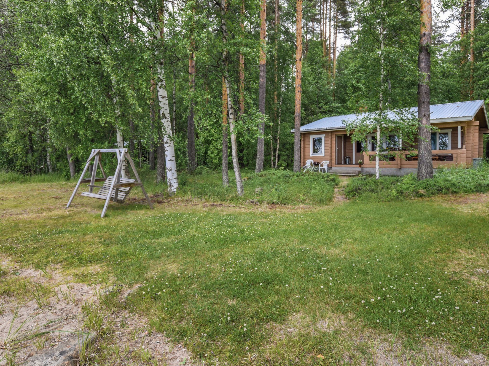 A wooden cabin with a porch, surrounded by a forest.