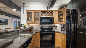 A modern kitchen with granite countertops, wooden cabinets, a black microwave, a stove, and a refrigerator. - Top of the Village~Ski-in/out~HT~Pool~Grill~Parking (Snowmass Village)