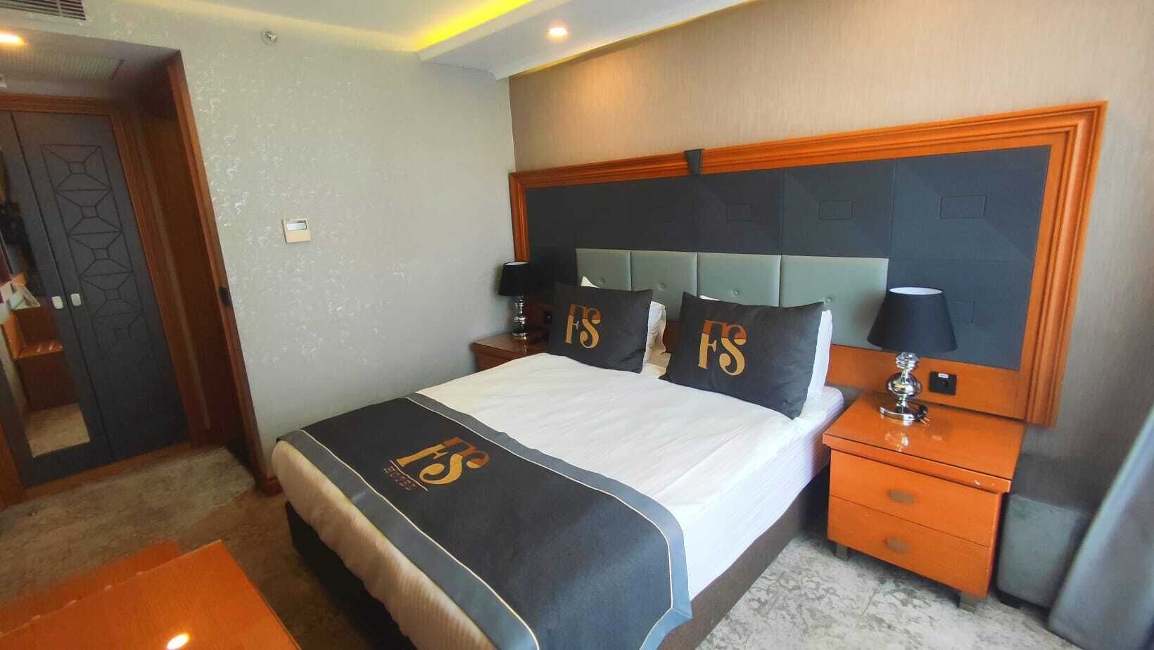 A hotel room with a bed, nightstands, a lamp, and a door.