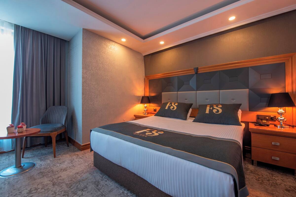 Hotellihuone, jossa on suuri sänky, kaksi yöpöytää, tuoli, pieni pöytä ja työpöytä.