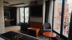 Hotellihuone, jossa on sänky, pieni puinen pöytä, tuoli, seinälle asennettu televisio ja parveke, jolta on näkymä kaupunkiin.