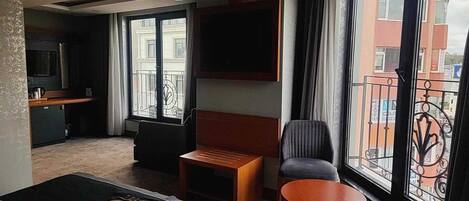 Una habitación de hotel con una cama, una pequeña mesa de madera, una silla, un televisor montado en la pared y un balcón con vistas a la ciudad.