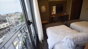 Hotellihuone, josta on näkymä kaupunkiin, huoneessa on työpöytä peilillä sekä kaksi sänkyä.