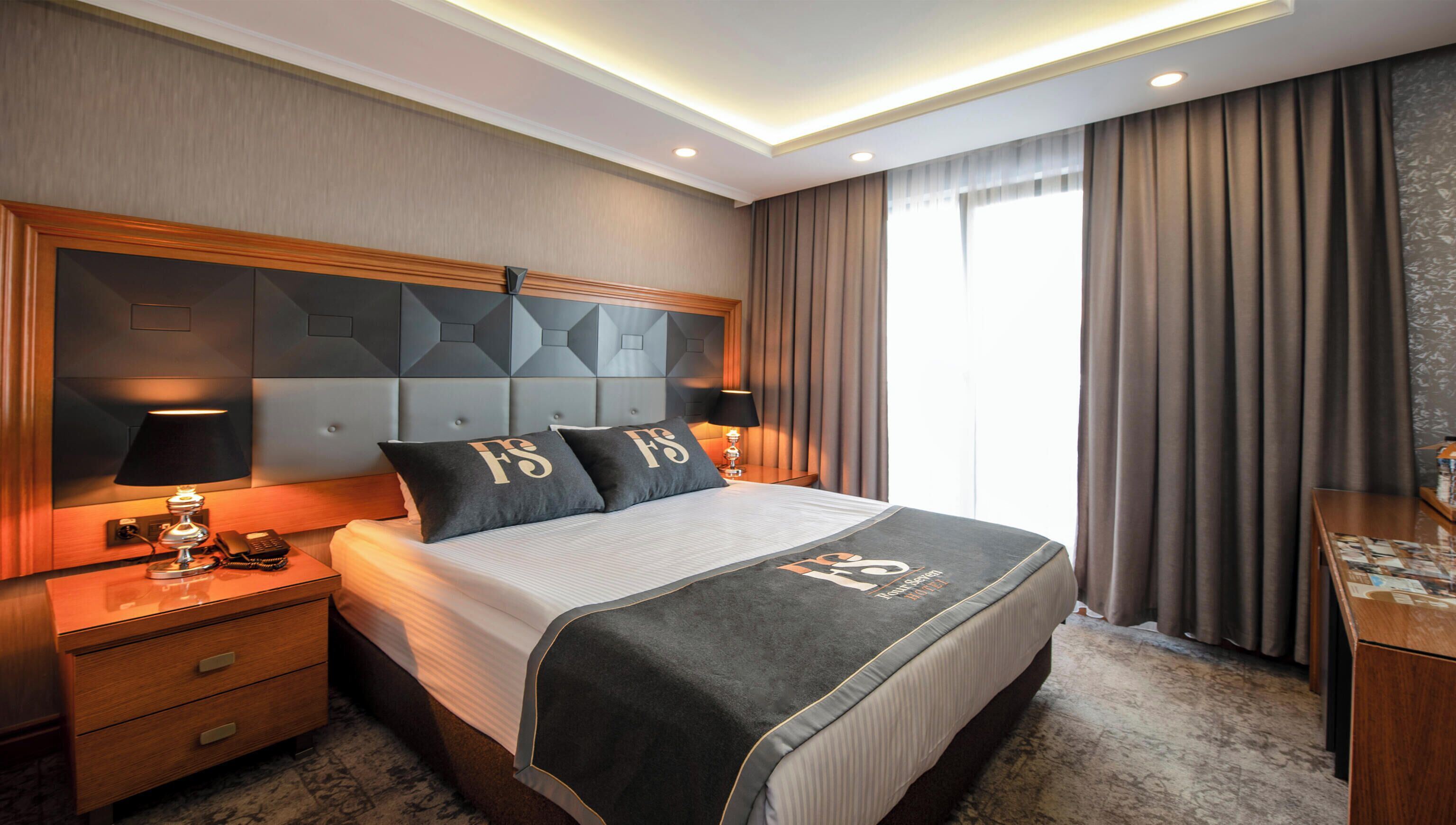 Una habitación de hotel con una cama grande, una mesita de noche con una lámpara y vistas al exterior.