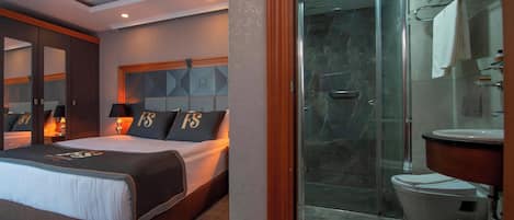 Habitación de hotel con cama, lámparas de noche, cabecera con diseños geométricos, zona de ducha con puerta de cristal y un inodoro.