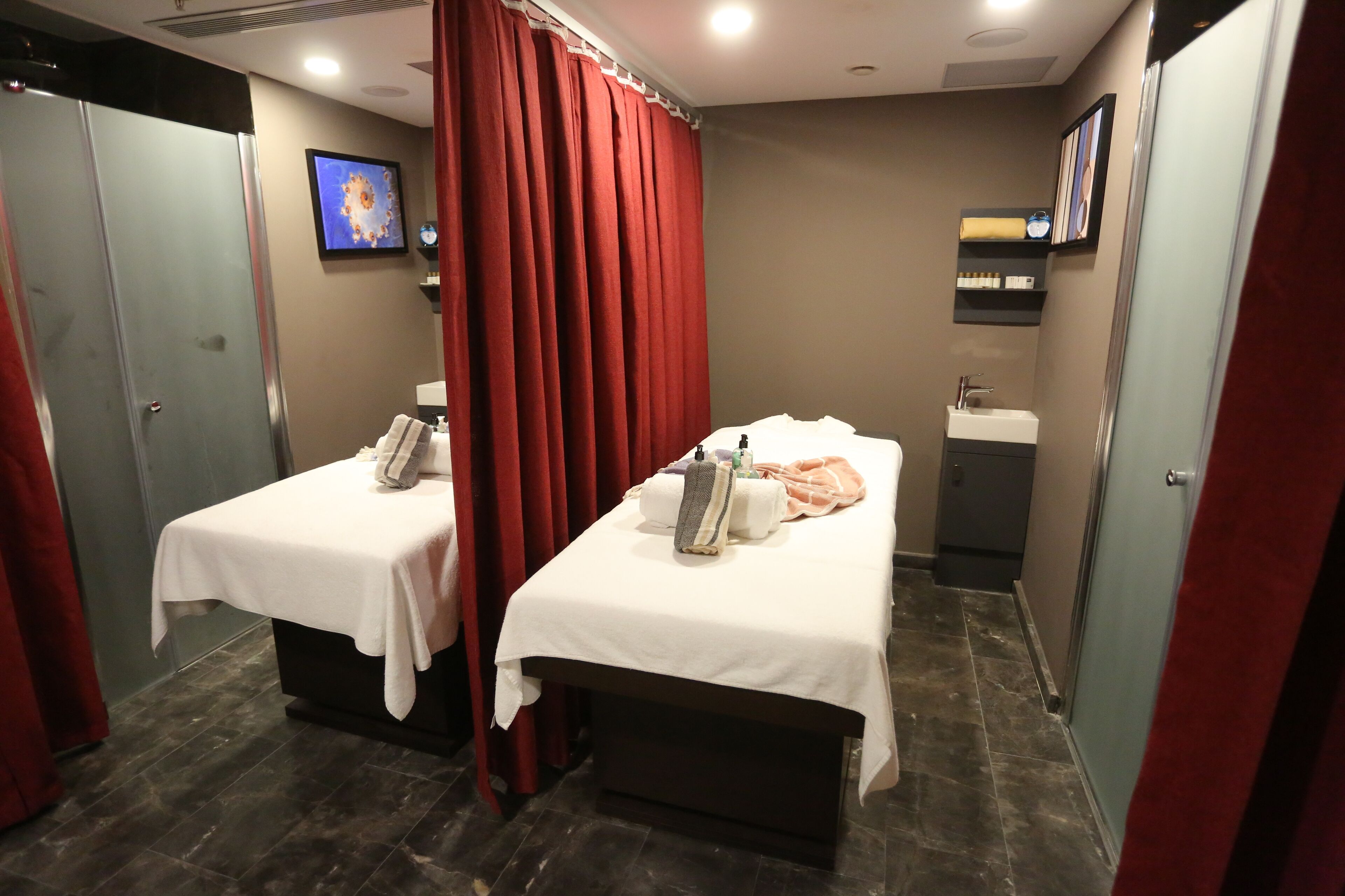 A hotel room with two beds, a bathroom, and a red curtain.