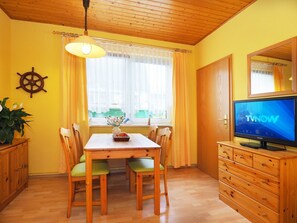 A dining area with a wooden table, chairs, a TV, and a cabinet. - Vacation apartment 1 - Uns Klausing (Heringsdorf)