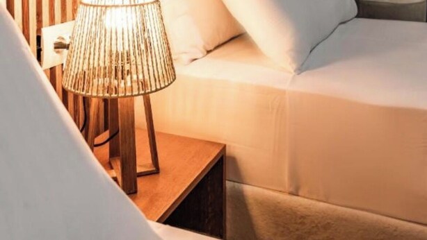 Un dormitorio con pared de listones de madera, cama con ropa de cama blanca y una lámpara de noche.