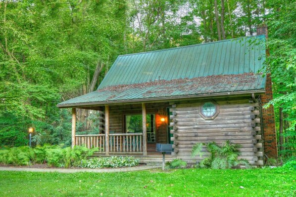 Un chalet rustique en rondins de bois, doté d’un porche et d’une cheminée, et entouré d’une végétation luxuriante.