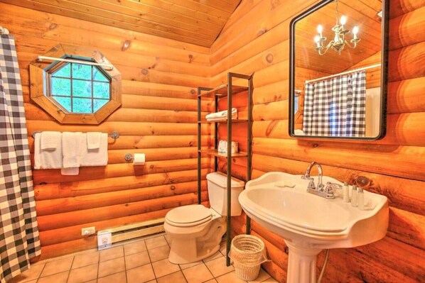 A wooden cabin bathroom with a toilet, sink, and a window above the toilet.
