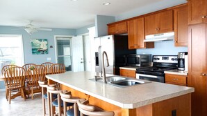 A kitchen with wooden cabinets, a stainless steel sink, a stove, and a microwave. There is a dining area with wooden chairs and a table. - Beachfront home cure for high blood pressure (Harbor Beach)