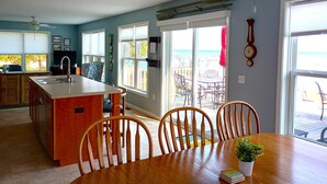A kitchen with a central island, wooden chairs, a dining table, and a view of the outdoors through large windows. - Beachfront home cure for high blood pressure (Harbor Beach)