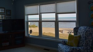 A room with a large window overlooking a beach, a ceiling fan, and a television on a wooden stand. - Beachfront home cure for high blood pressure (Harbor Beach)