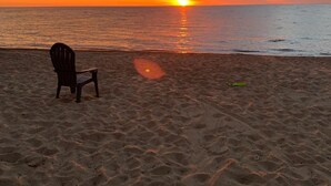 A beach with a chair and a pair of sandals on the sand, facing the ocean at sunset. - Beachfront home cure for high blood pressure (Harbor Beach)