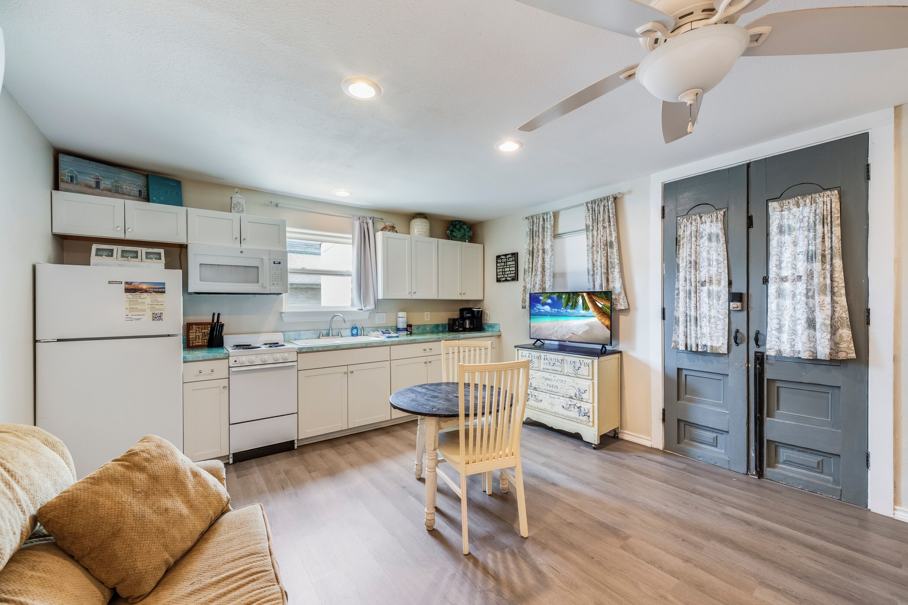 A compact kitchen with a dining table, chairs, a microwave, a refrigerator, and a ceiling fan.