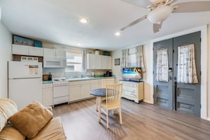 Une cuisine compacte comprenant une table à manger, des chaises, un four à micro-ondes, un réfrigérateur et un ventilateur de plafond.