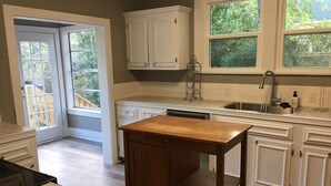 A kitchen with white cabinetry, a wooden table, and a dishwasher. - Back to School Special! 5 minutes from Majestic Baseball Fields (Hot Springs)