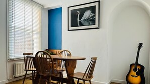 Zona pranzo con un tavolo rotondo in legno e sei sedie, un quadro con un cigno appeso al muro e una chitarra appoggiata al muro.