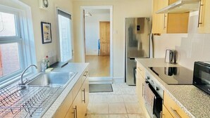 Una cucina con frigorifero in acciaio inossidabile, forno integrato e microonde. Una finestra offre luce naturale e un'apertura conduce in un'altra stanza.
