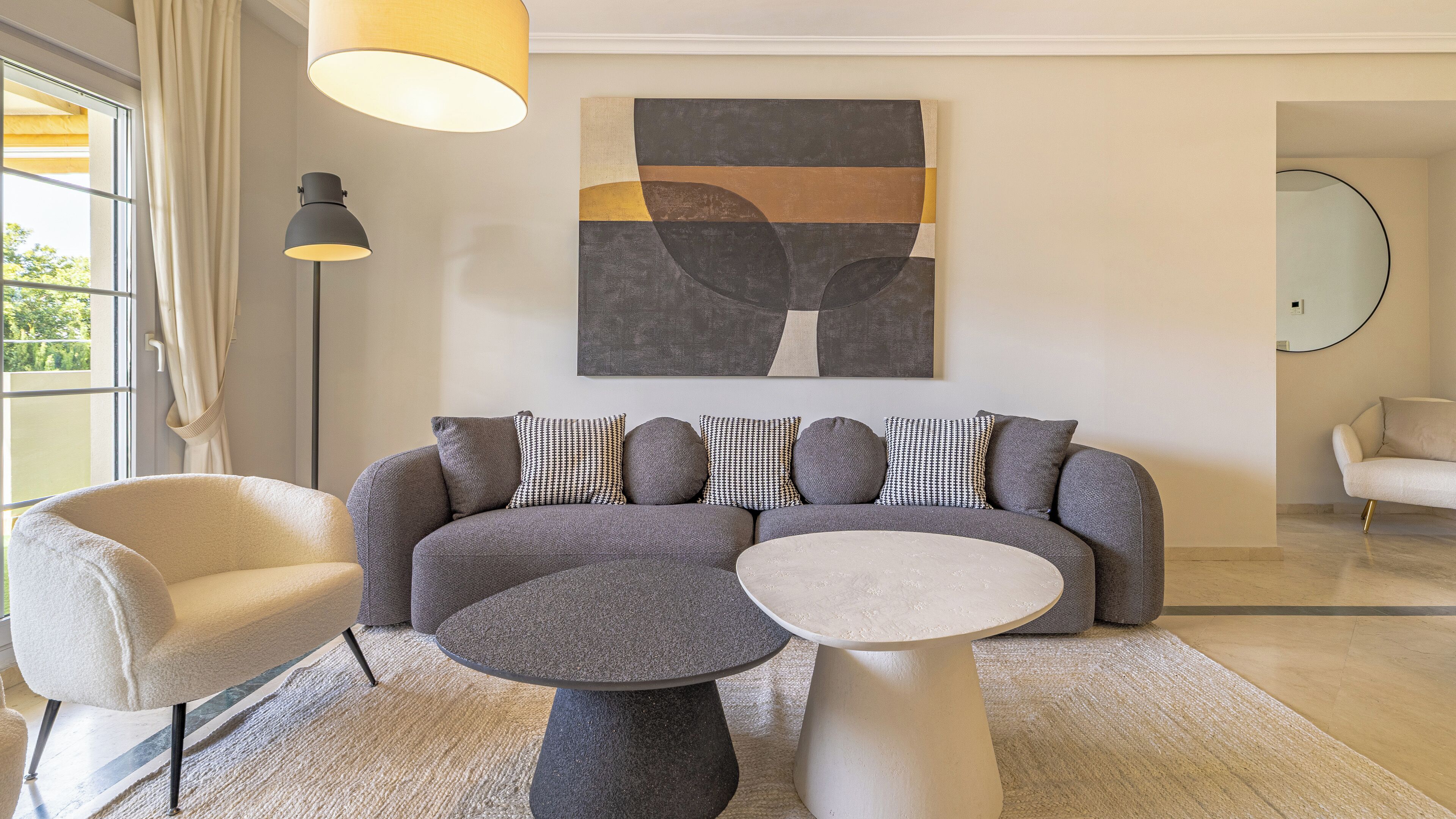 Una sala de estar moderna con un sofá gris, una mesa redonda de centro y dos sillones. Un cuadro abstracto de gran tamaño cuelga sobre el sofá.