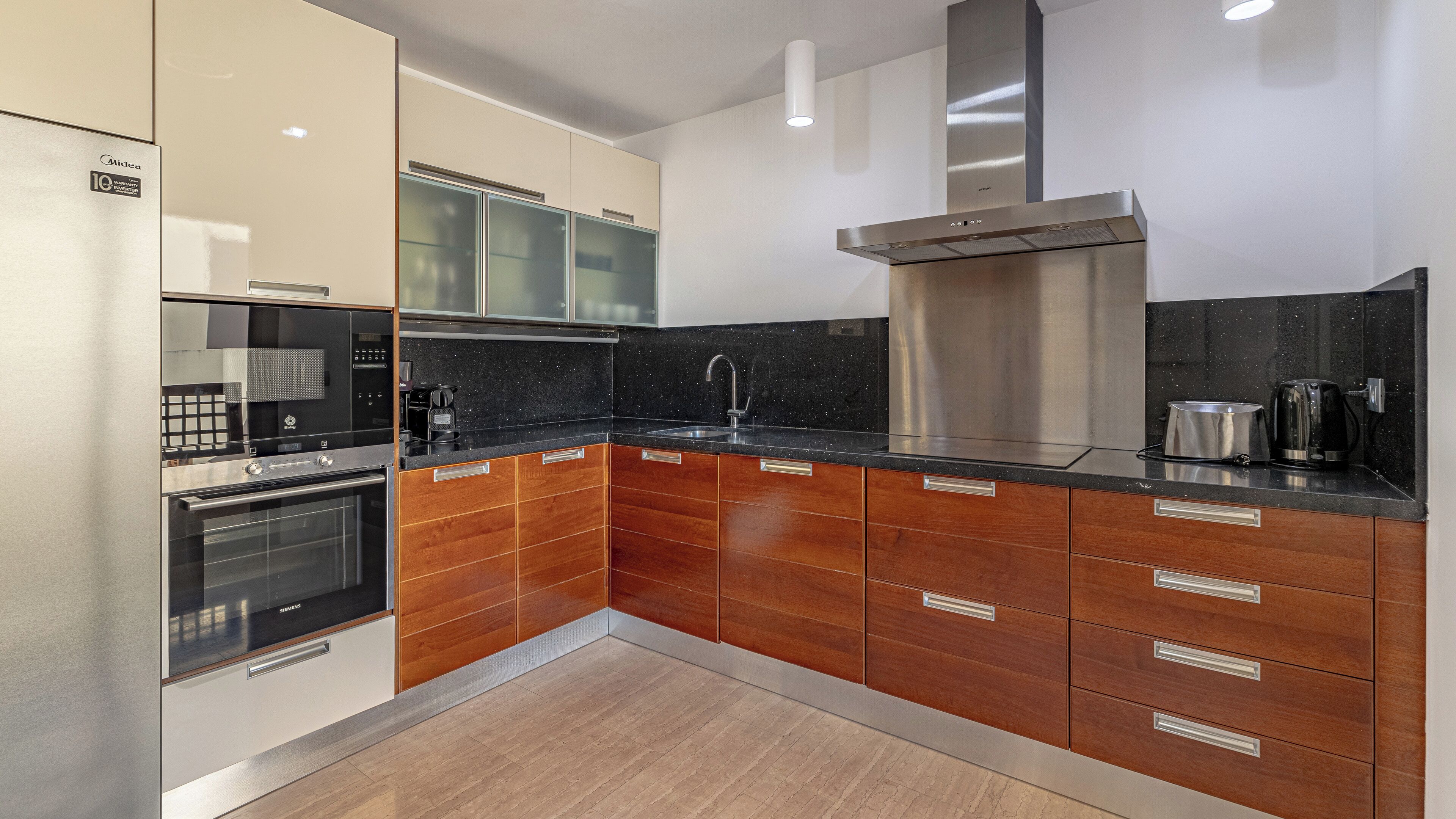 A modern kitchen with stainless steel appliances, wooden cabinetry, and a black granite countertop.