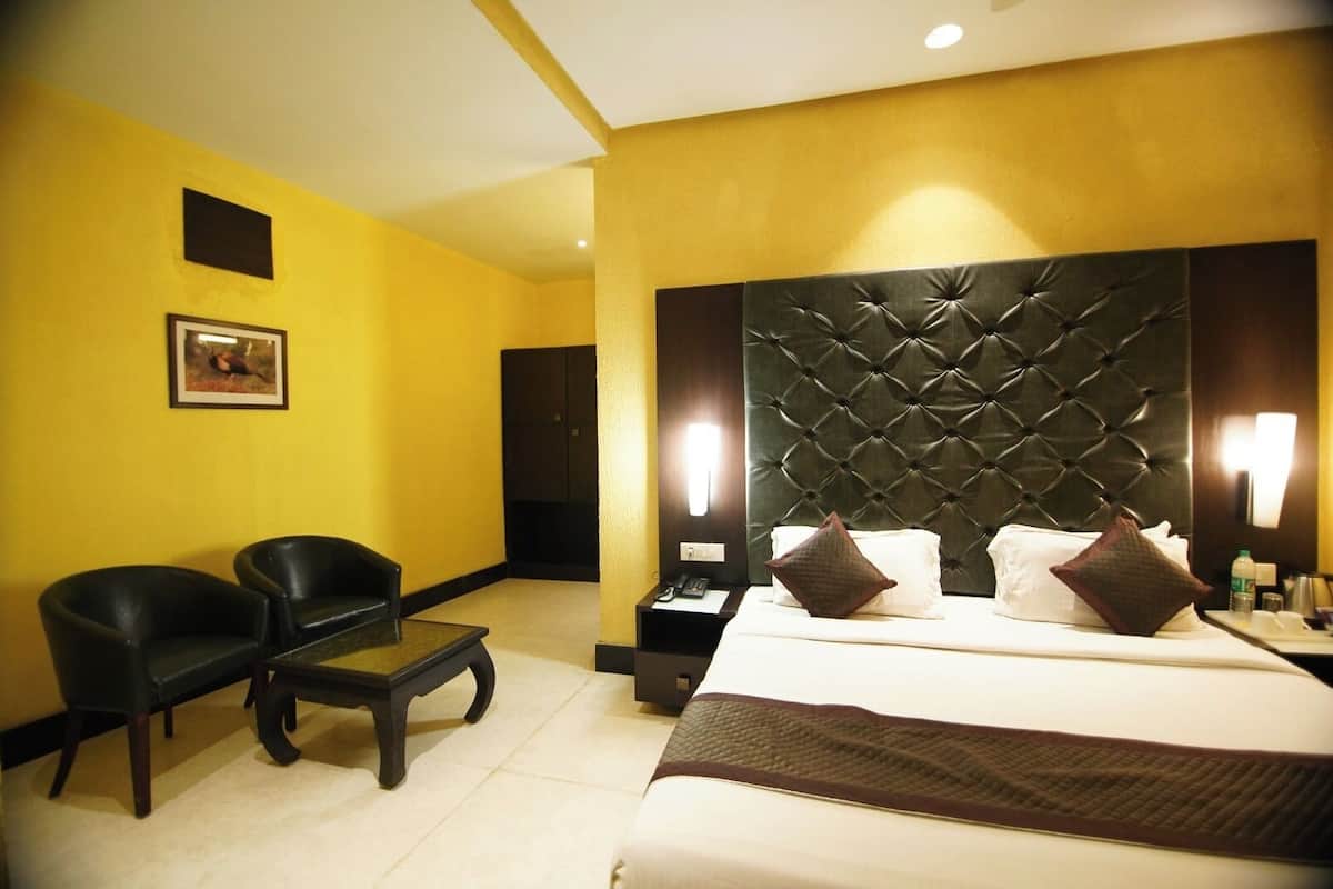A hotel room with a large bed, two black chairs, a small table, and a wall-mounted TV.