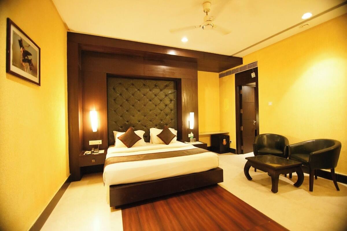 A hotel room with a large bed, a wooden headboard, two bedside tables, a desk, a chair, and a ceiling fan.
