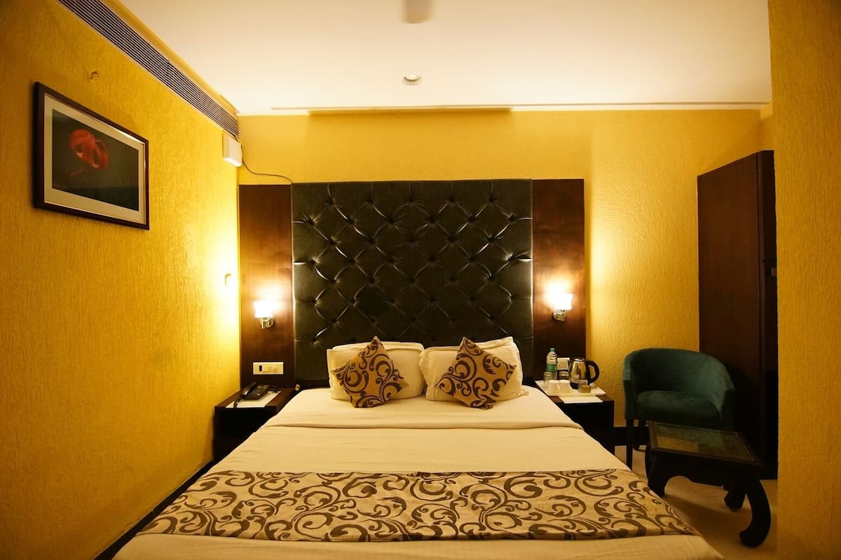 A hotel room with a large bed, a tufted headboard, bedside lamps, a green armchair, and a framed picture on the wall.
