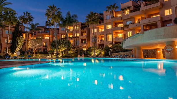 A hotel with a swimming pool, palm trees, and multiple balconies.