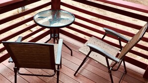 A wooden deck with a round glass table and two metal chairs. - Newly built quiet studio apartment near Reversing Falls (Blue Hill)