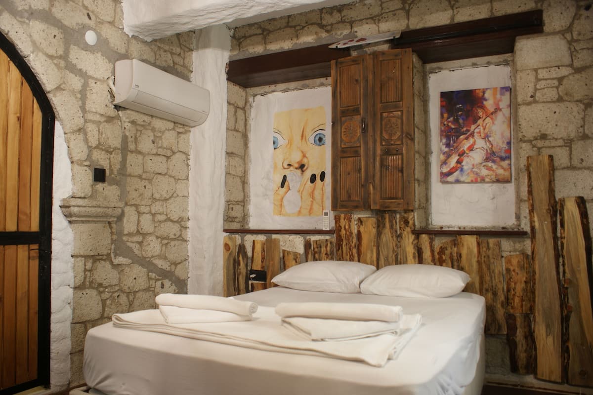 Una habitación con pared de piedra, puerta de madera y cama con ropa blanca.
