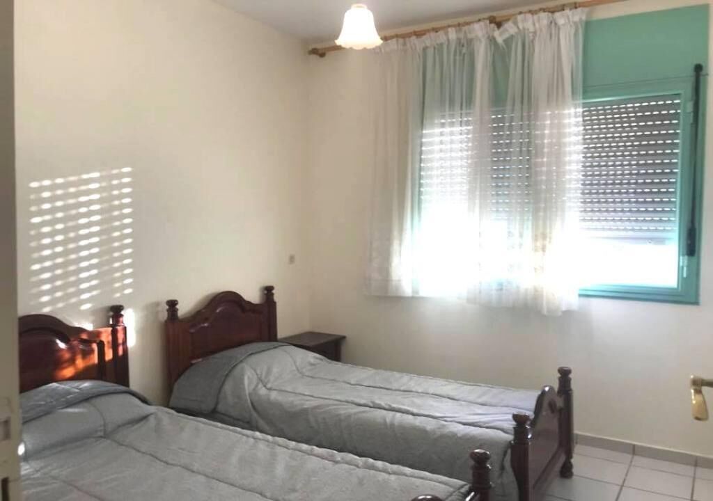 Una camera da letto con due letti singoli, una finestra con tende, un comodino e una lampada a sospensione.