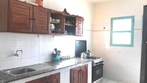 Una cocina con paredes de azulejos blancos, armarios de madera, una estufa y un ventanal.