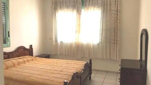 Un dormitorio con cama, cómoda y ventana con cortinas.