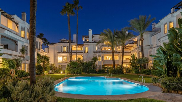 Un grand hôtel à plusieurs étages, doté d’une piscine entourée d’une végétation luxuriante et de palmiers.