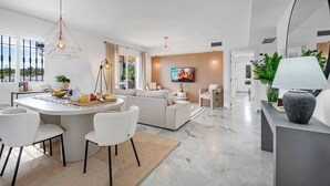 Un salon moderne avec un coin repas, comprenant un grand téléviseur, des sièges confortables et une vue sur l’extérieur.