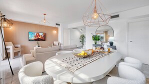 Un salon moderne doté d’une grande table à manger blanche, de sièges confortables, d’un téléviseur à écran plat et d’une grande fenêtre.
