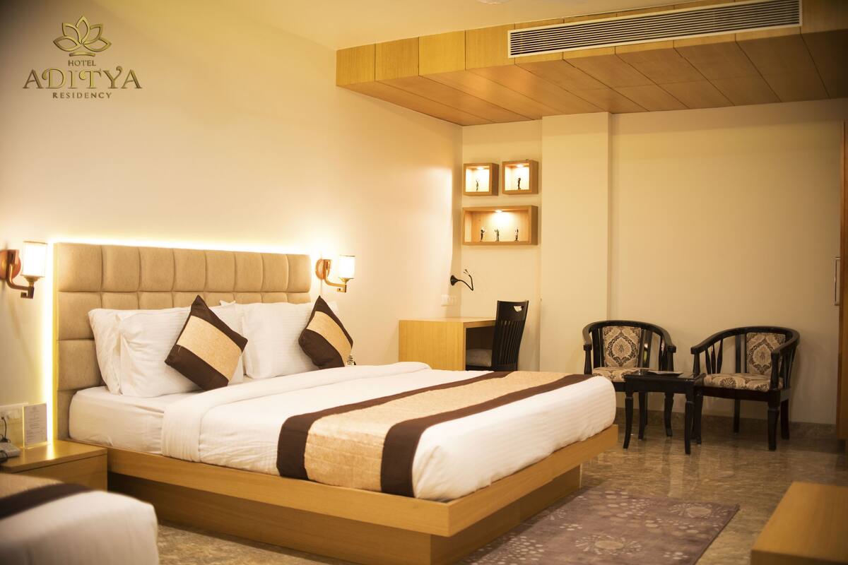 Une chambre d’hôtel avec un grand lit, des tables de chevet, un bureau, deux chaises et une étagère fixée au mur, équipée de lampes.