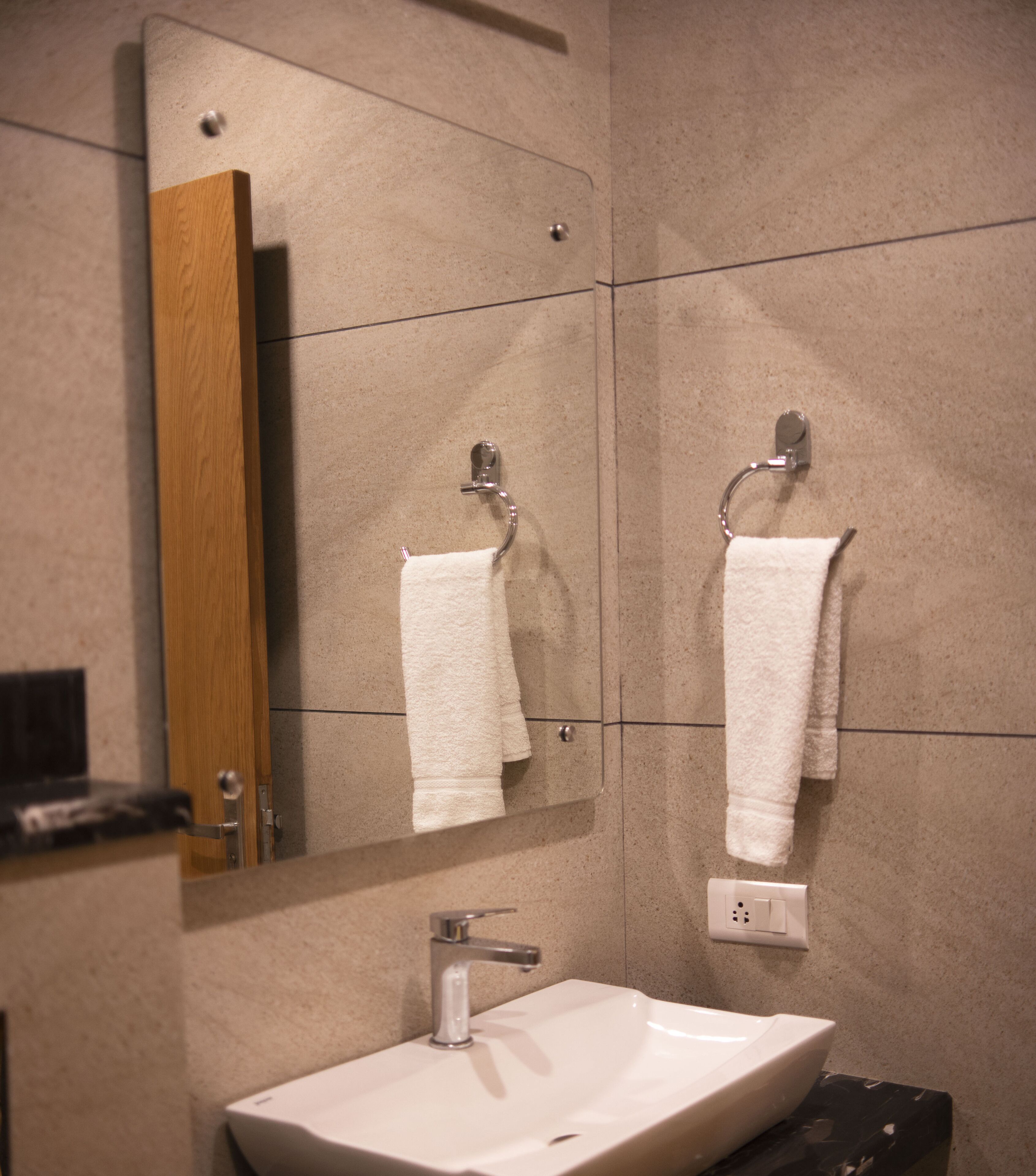 Un baño con un lavamanos blanco, un espejo y dos toallas colgadas en ganchos.