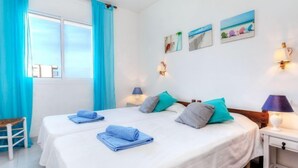 Ein Hotelzimmer mit zwei Betten, einem Fenster mit blauen Vorhängen und Wandbildern.