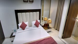 A hotel room with a large bed, two pillows, a nightstand with a lamp, and a mirror on the wall. - Hotel Western (Bhopal)