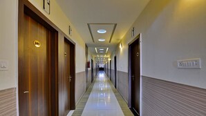 A hotel corridor with wooden doors, a tiled floor, and recessed lighting. - Hotel Western (Bhopal)