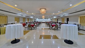 A spacious banquet hall with round tables and chairs, a chandelier, and a tiled floor. - Hotel Western (Bhopal)