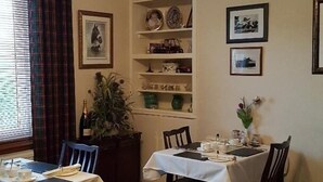 Ein Essbereich mit zwei Tischen für vier Personen, einer Bücherwand mit Dekoration und einem Fenster mit Vorhängen.