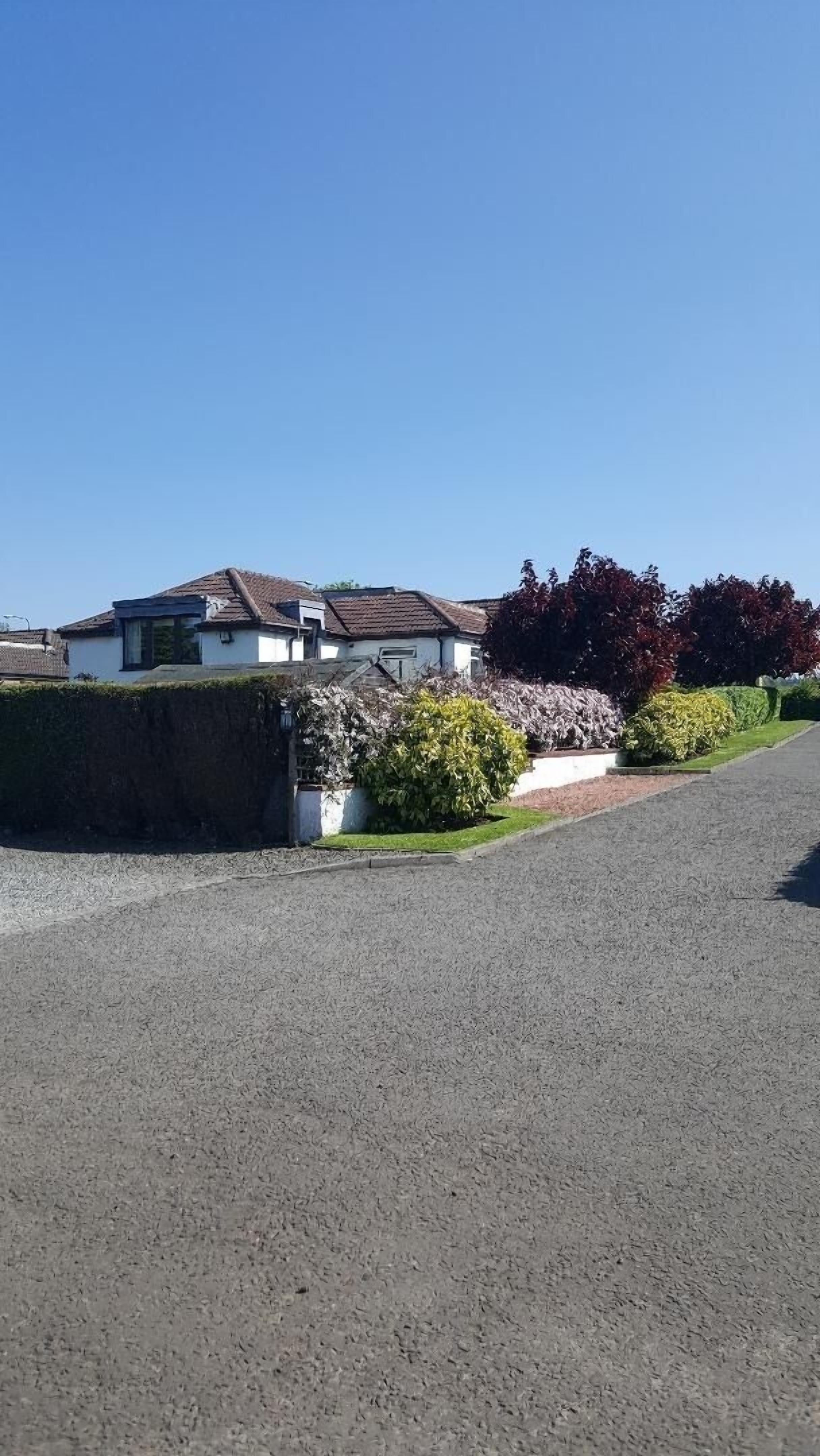 A residential property with a white house, a driveway, and a well-maintained garden with various shrubs and a lawn.