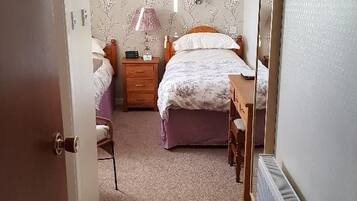 Ein Schlafzimmer mit einem Doppelbett, einem Nachttisch, einem Sessel, einem Heizkörper und einer Tür zu einem anderen Raum.